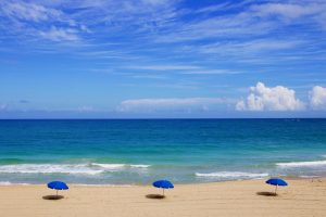 Blue umbrellas on the sand with waves crashing