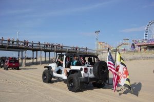 White wrangler Jeep on beach with American Flag and Maryland Flag on the back