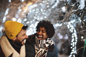 Two people laughing with snow and lights behind them